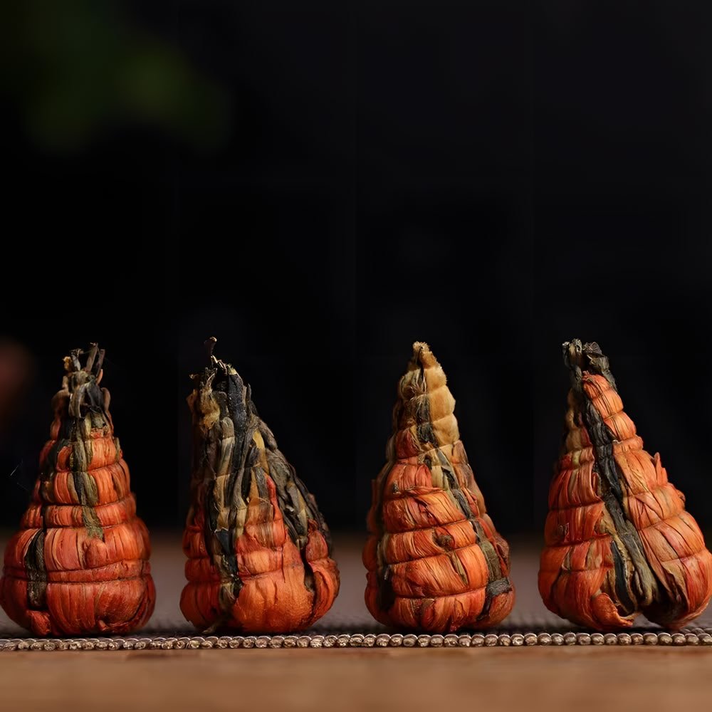 A detailed macro shot of four dry Lily Pagoda Bloom bundles standing against a black background. The image highlights the tight, hand-sewn structure showing dark Dianhong tea leaves wrapped securely by dry lily flower fibers into a pagoda shape.