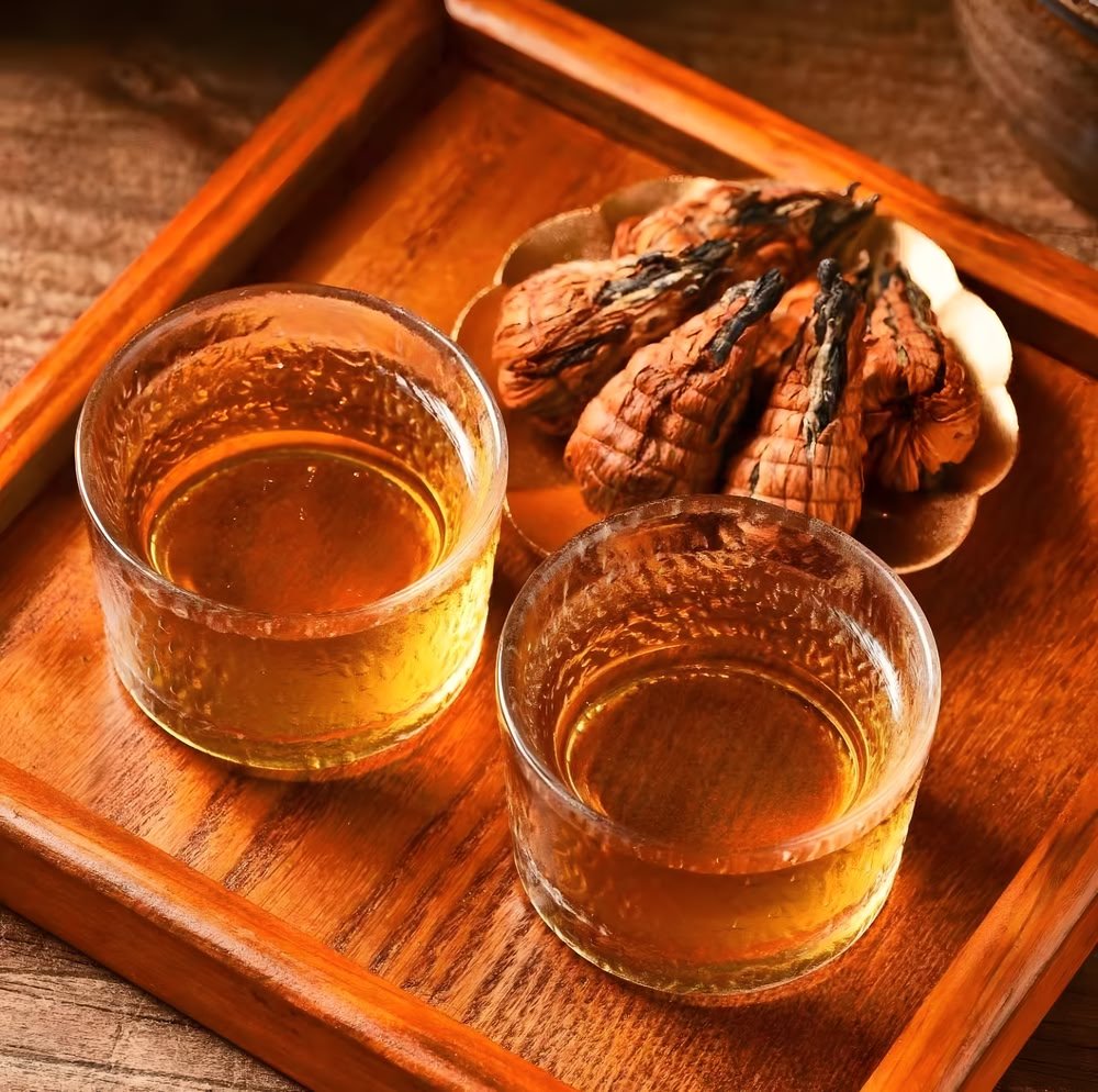 A warm, inviting lifestyle photograph of a wooden serving tray. It holds two glass cups holding brewed amber-colored Dianhong flowering tea and a small brass dish with dry Pagoda bundles, ready for a relaxing tea break.