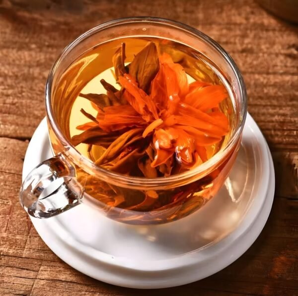 Close-up view of a clear glass cup holding a fully unfurled Lily Pagoda Bloom. Vibrant orange lily petals reveal a heart of dark Dianhong black tea leaves. The tea liquor is a rich, warm amber color, set on a rustic wooden table.