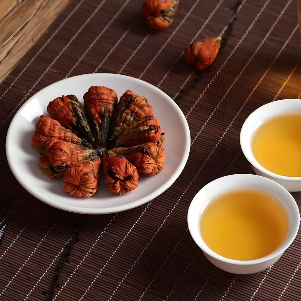 A white ceramic plate displaying dry, cone-shaped "Pagoda" bundles of lily and Dianhong black tea. Beside it are two white tasting cups filled with clear, bright orange-yellow Yunnan red tea soup. The setting is a dark bamboo mat.