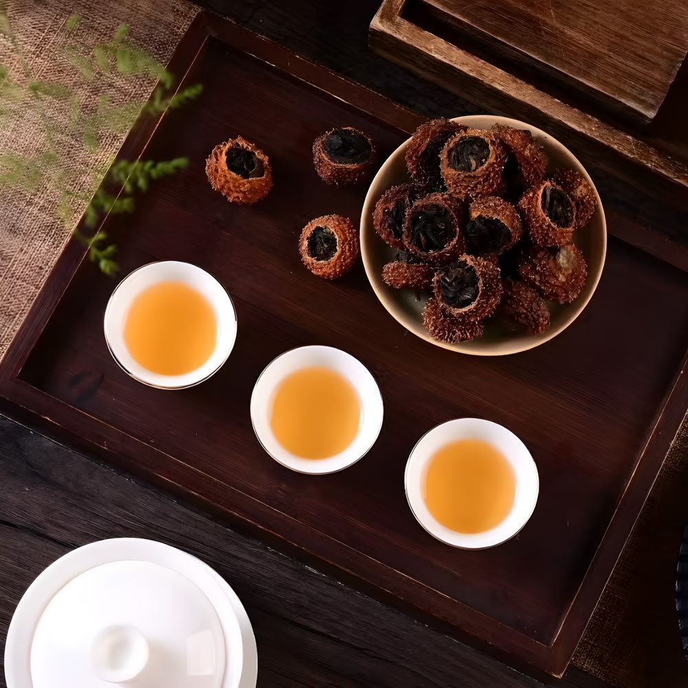 A tea serving setup on a dark wooden tray, featuring three cups of brewed golden tea and a pile of dried Chestnut Rose fruits stuffed with black tea.