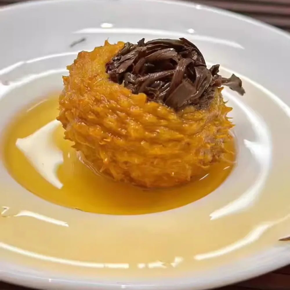 Close-up customer photo of a rehydrated Chestnut Rose fruit sitting in a white saucer after brewing. The wet fruit peel is golden orange, filled with expanded dark tea leaves.