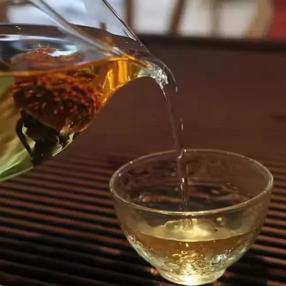 Action shot from a customer review showing clear golden Chestnut Rose tea being poured from a pitcher into a small glass tasting cup.