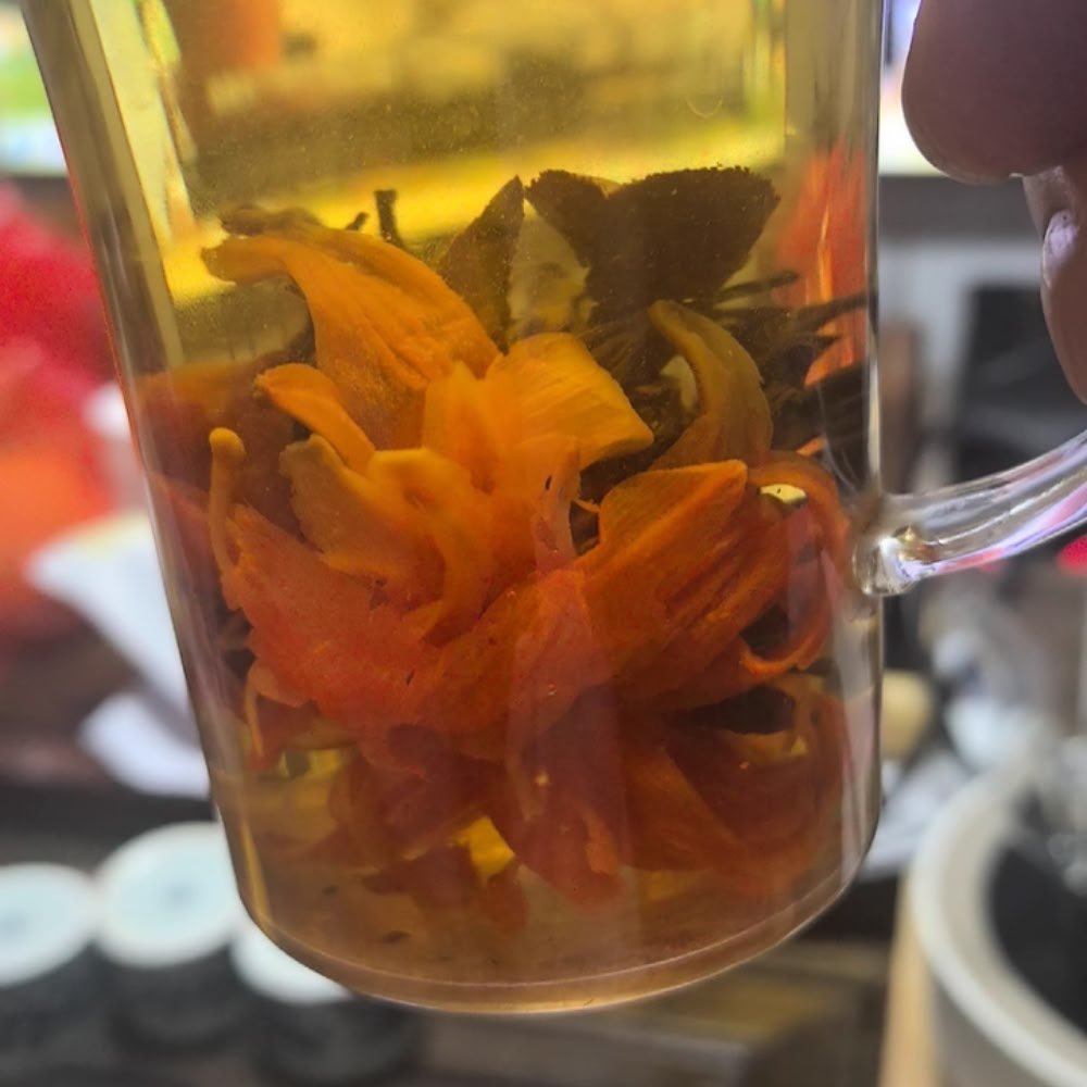 A side view of the Lily Pagoda Bloom black tea flower fully expanded in a transparent glass, showing its vibrant petals and strong floral presence.