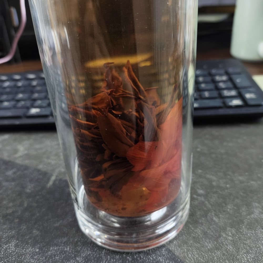 Steeping Lily Pagoda Bloom in a tall glass, showing the artisanal black tea leaves and lily petals unfurling to release a honey-like aroma.