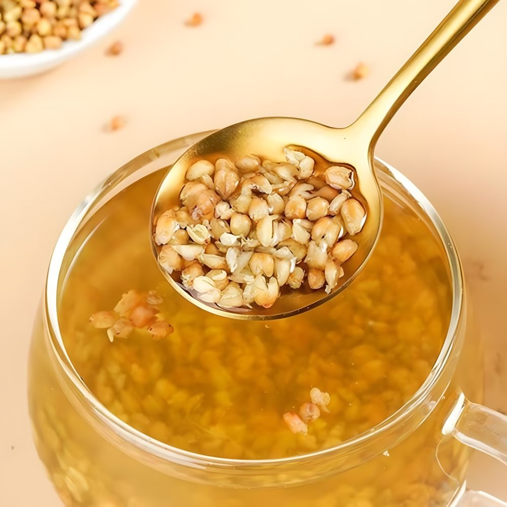 An elegant golden spoon lifting plump, soft, and chewy steeped Nutty Tartary Buckwheat kernels from a clear glass of golden tea liquor.