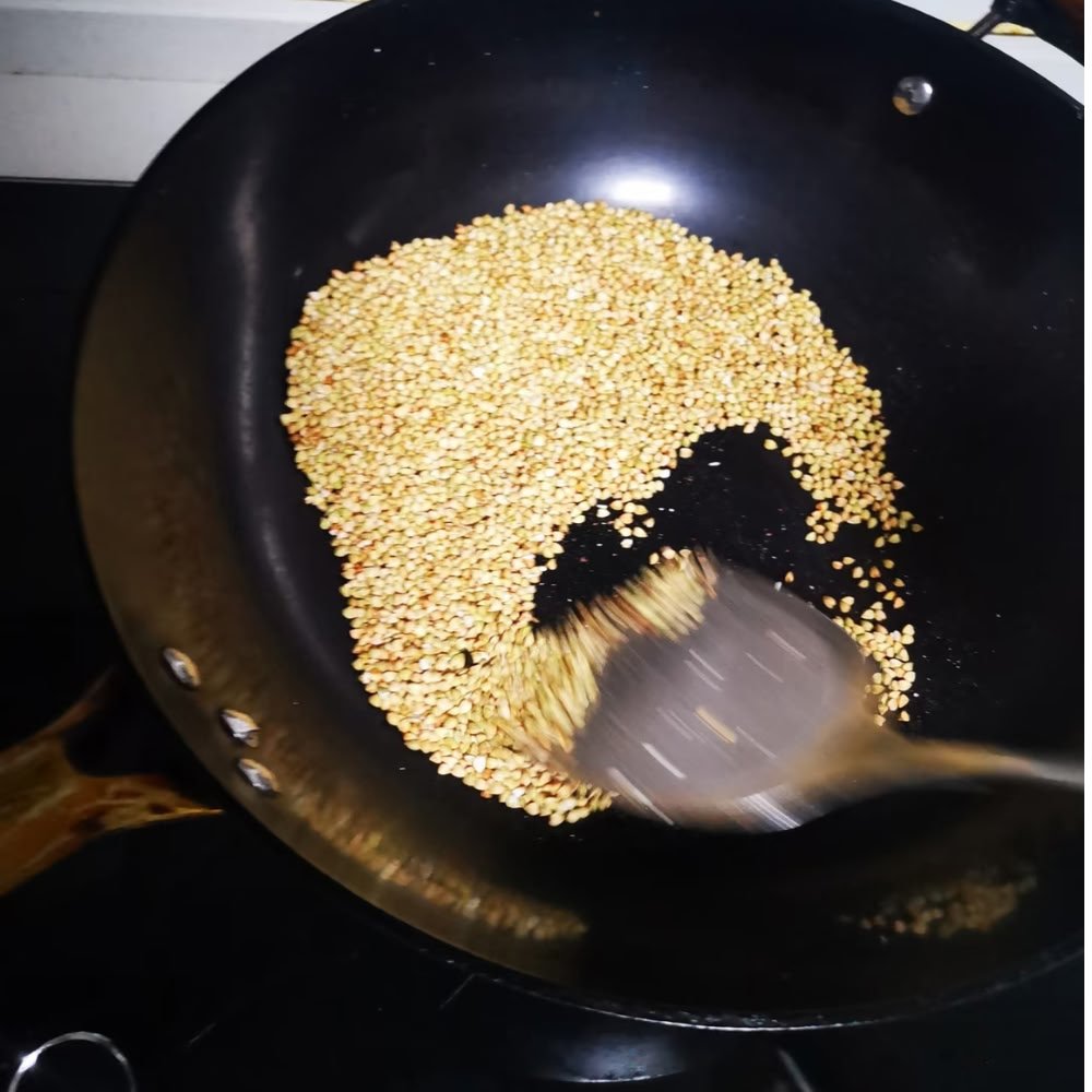 A dynamic shot of raw Nutty Tartary Buckwheat kernels being gently roasted in a traditional dark wok, tossed with a spatula to ensure an even, clean toasty aroma.