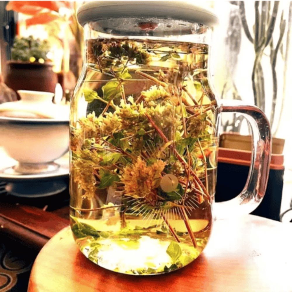 A clear glass mug filled with a pale-yellow Xiangru Sprig infusion and fully steeped herbs, representing a clean and hydrating palate cleanser.