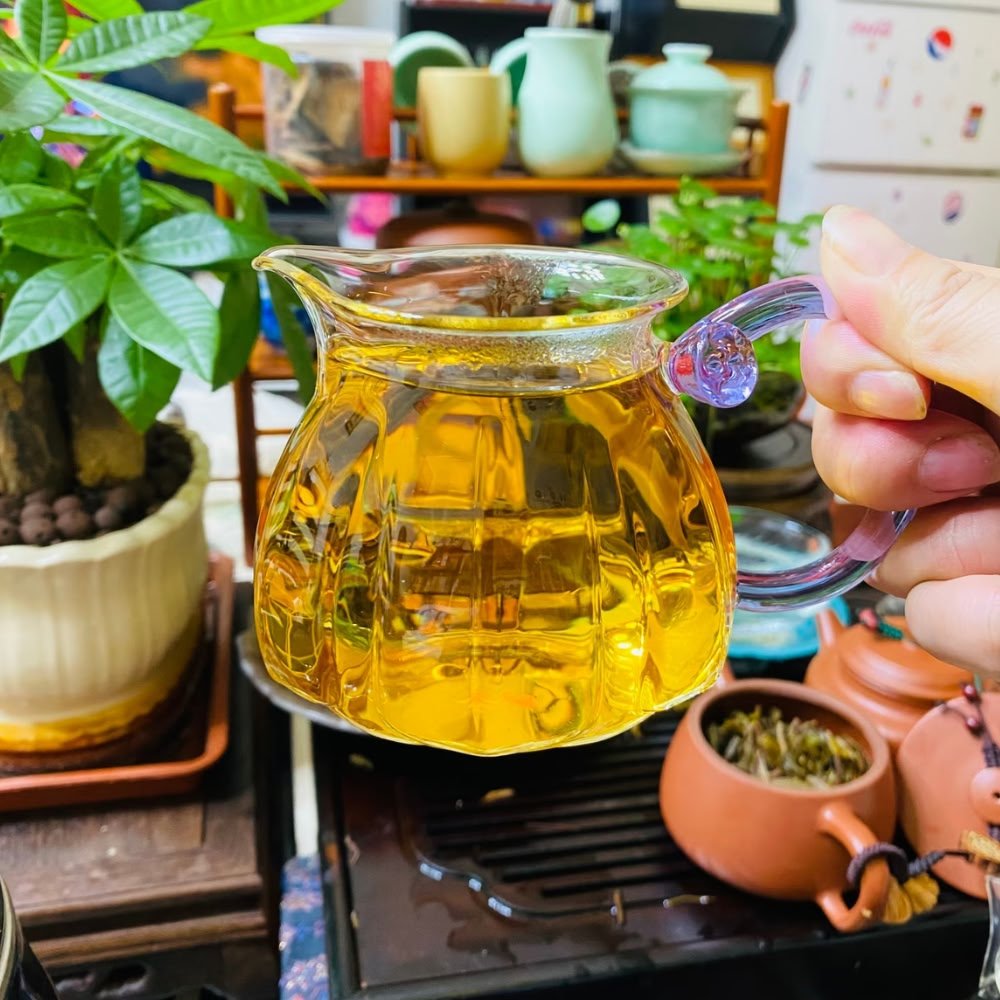 A customer photo holding a glass pitcher filled with golden Dongzisu tea liquor, with traditional clay teapots and plants in the background.