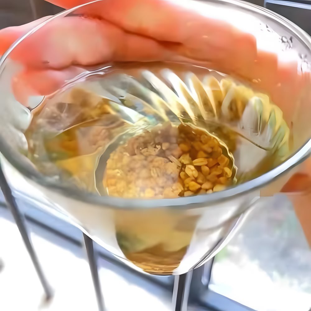 A close-up customer photo holding a clear glass cup filled with golden Nutty Tartary Buckwheat tea and steeped kernels, catching the sunlight.