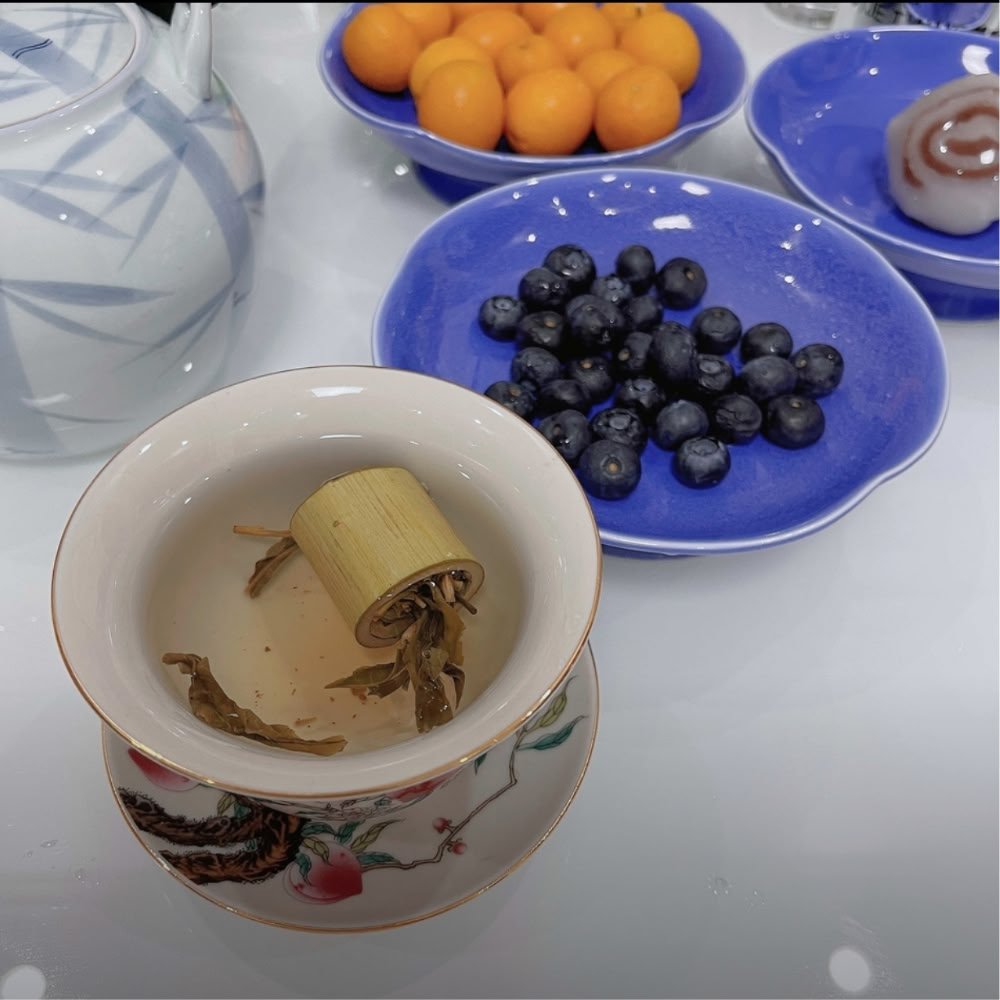 A beautiful customer lifestyle photo featuring Bamboo Dew tea steeping in a delicate porcelain cup, paired with fresh blueberries and kumquats.