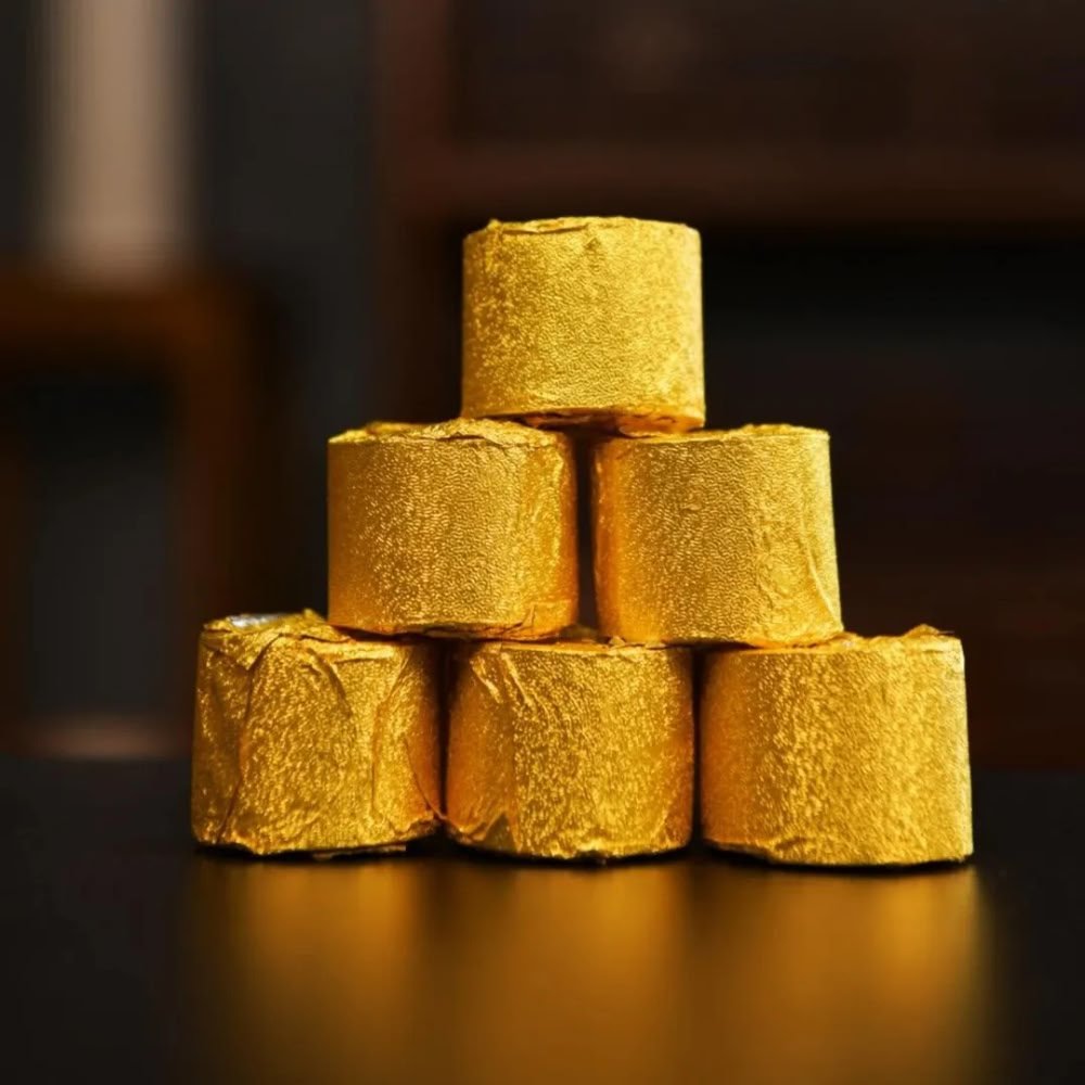 A pyramid stack of premium Bamboo Dew tea portions, each tightly wrapped in stunning gold foil to preserve its delicate aroma and prevent moisture loss.