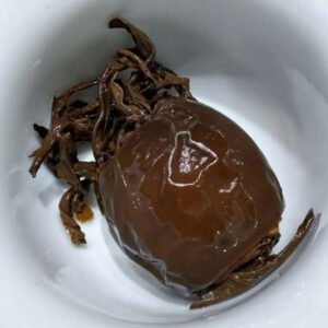 Extreme macro photography capturing the rich, deep wrinkled texture of aged dried tamarillo (tree tomato) husks tightly bound to the premium dark tea leaves inside, showcasing the artisan quality.