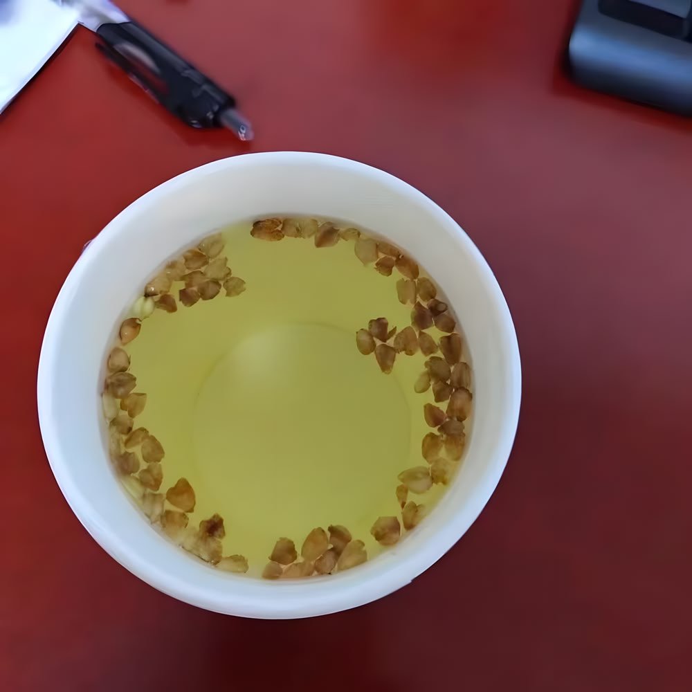 Top-down customer photo of Nutty Tartary Buckwheat kernels steeping in a white cup on a reddish office desk.