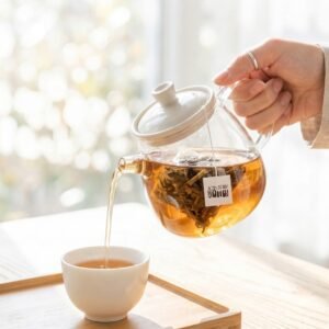 A sunlit aesthetic scene showing a hand pouring clear, golden Dongzisu herbal tea from a glass teapot into a delicate white porcelain cup.