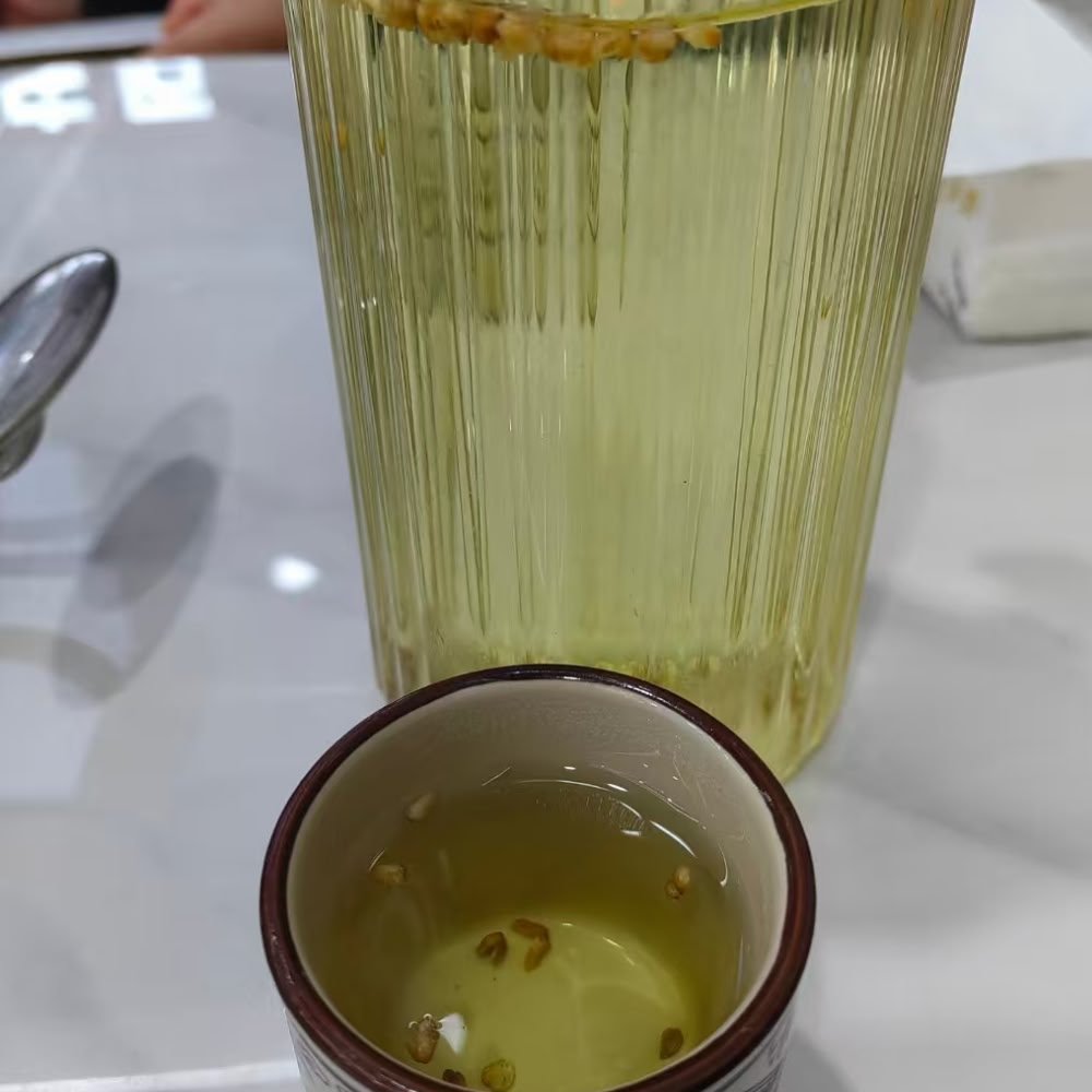 A tall fluted glass and a small traditional ceramic cup filled with golden Nutty Tartary Buckwheat tea on a white table setting.